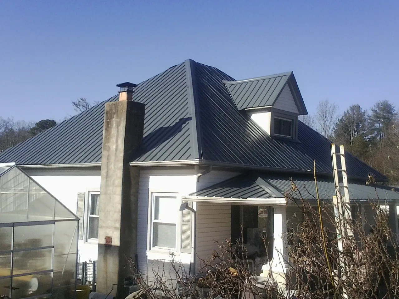 Dark blue standing seam metal roof on a white farmhouse with dormer — Slate & Tile Roof Repair by Roofing Brothers in Falls