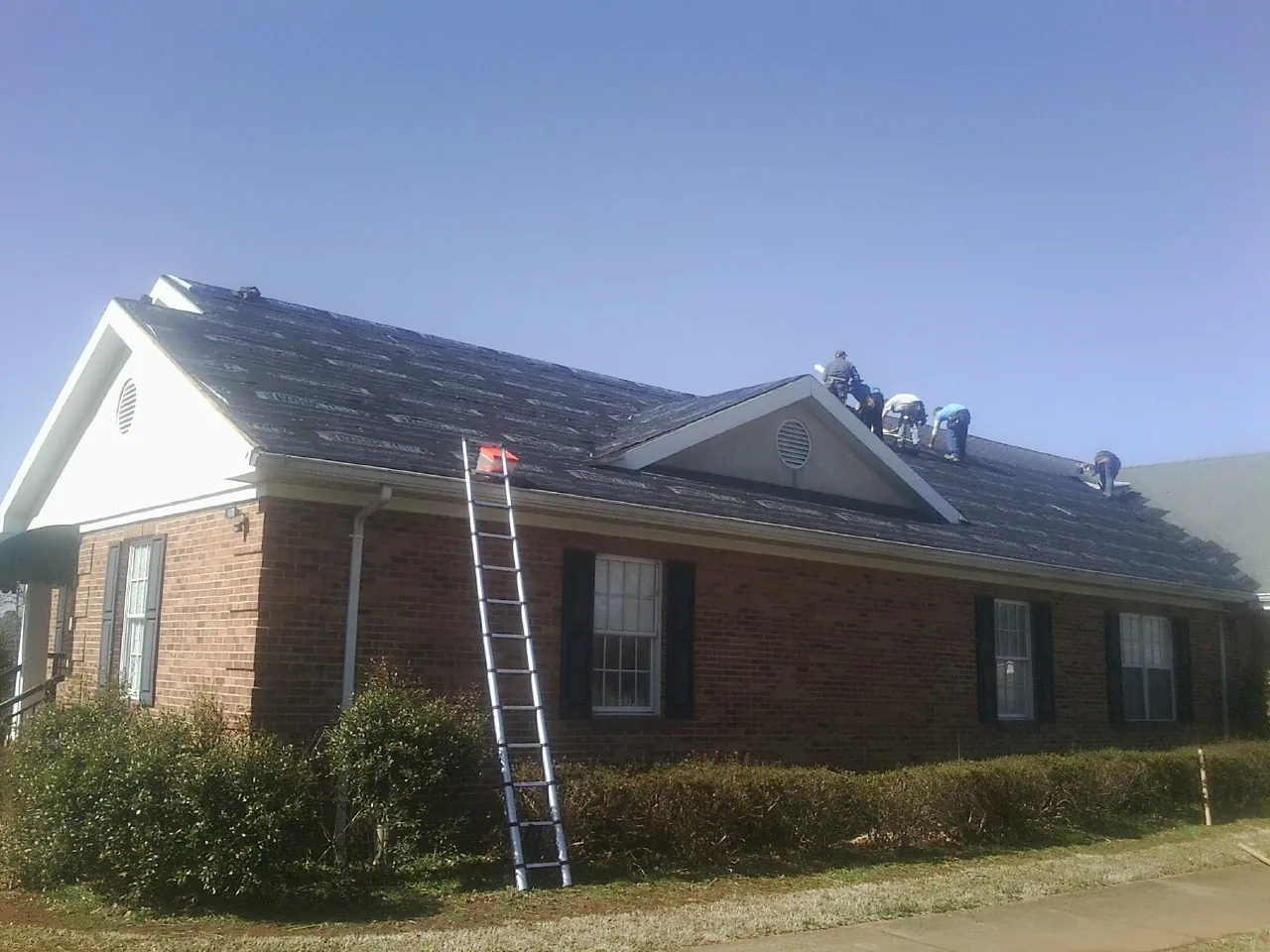 Crew tearing shingles off a brick ranch roof with a ladder set — Emergency Roof Repair work by our crew in Falls