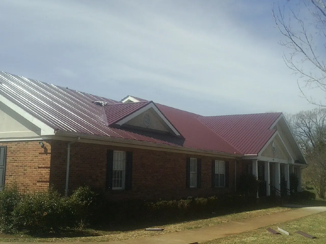 Red metal roof with gabled entries on a long brick building, from a Hail Damage Roof Repair job in Falls