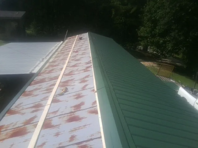 Old rusted panels beside newly installed green metal roofing — Wind Damage Roof Repair by Roofing Brothers in Falls