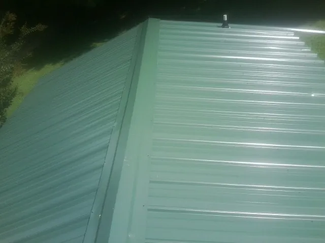 New green metal panels meeting at the ridge of a roof — Flat Roof Repair work by our crew in Falls