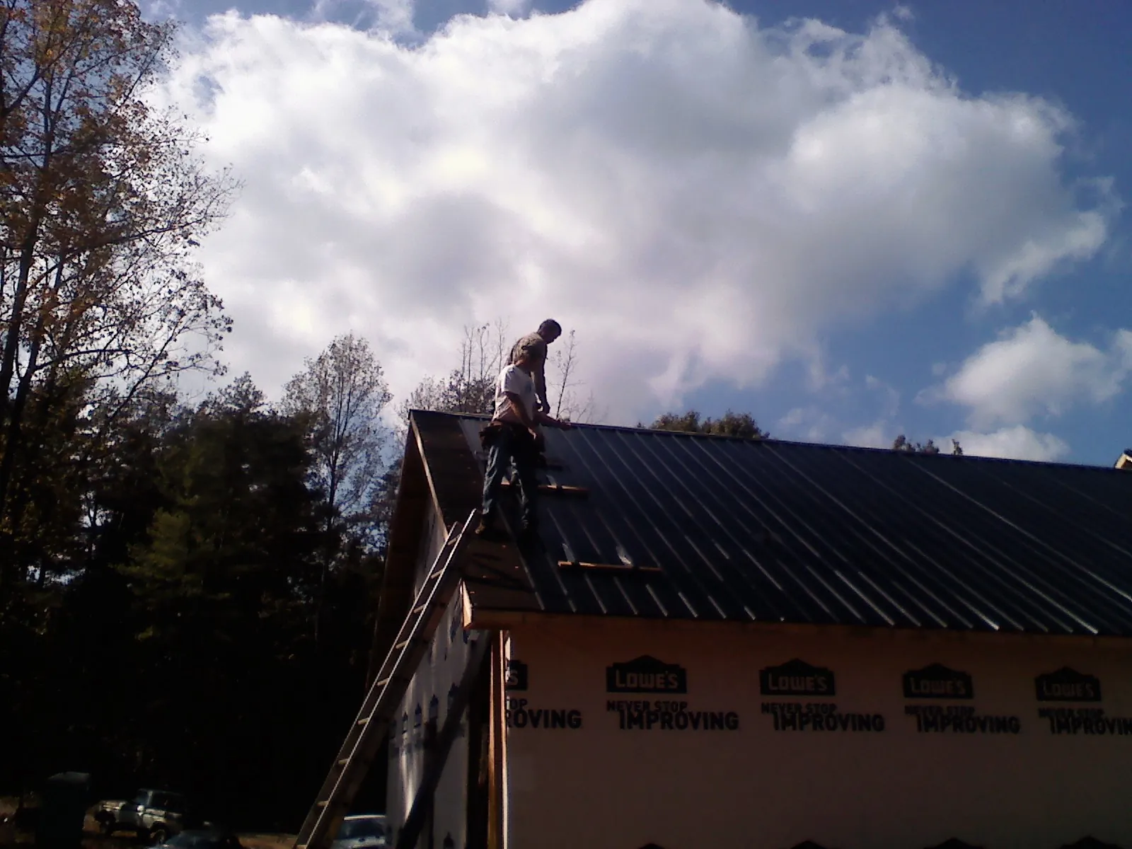 Roofer fastening dark metal panels high against a cloudy sky, from a Roof Inspection job in Falls
