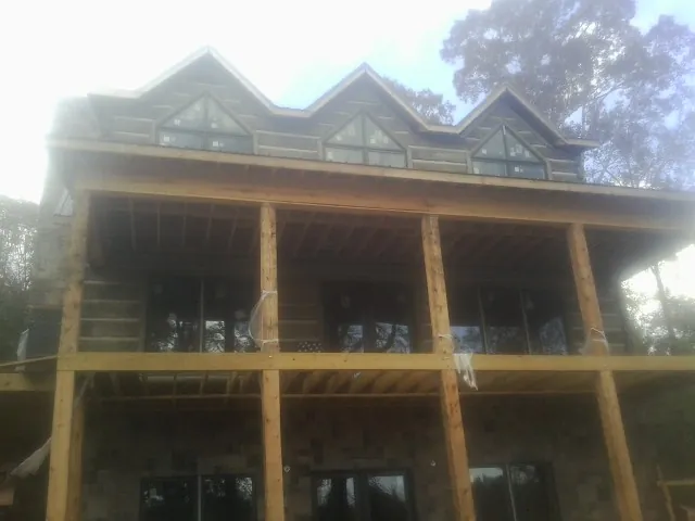 Dormers and porch framing on a large log home under construction — Roof Coating work by our crew in Falls