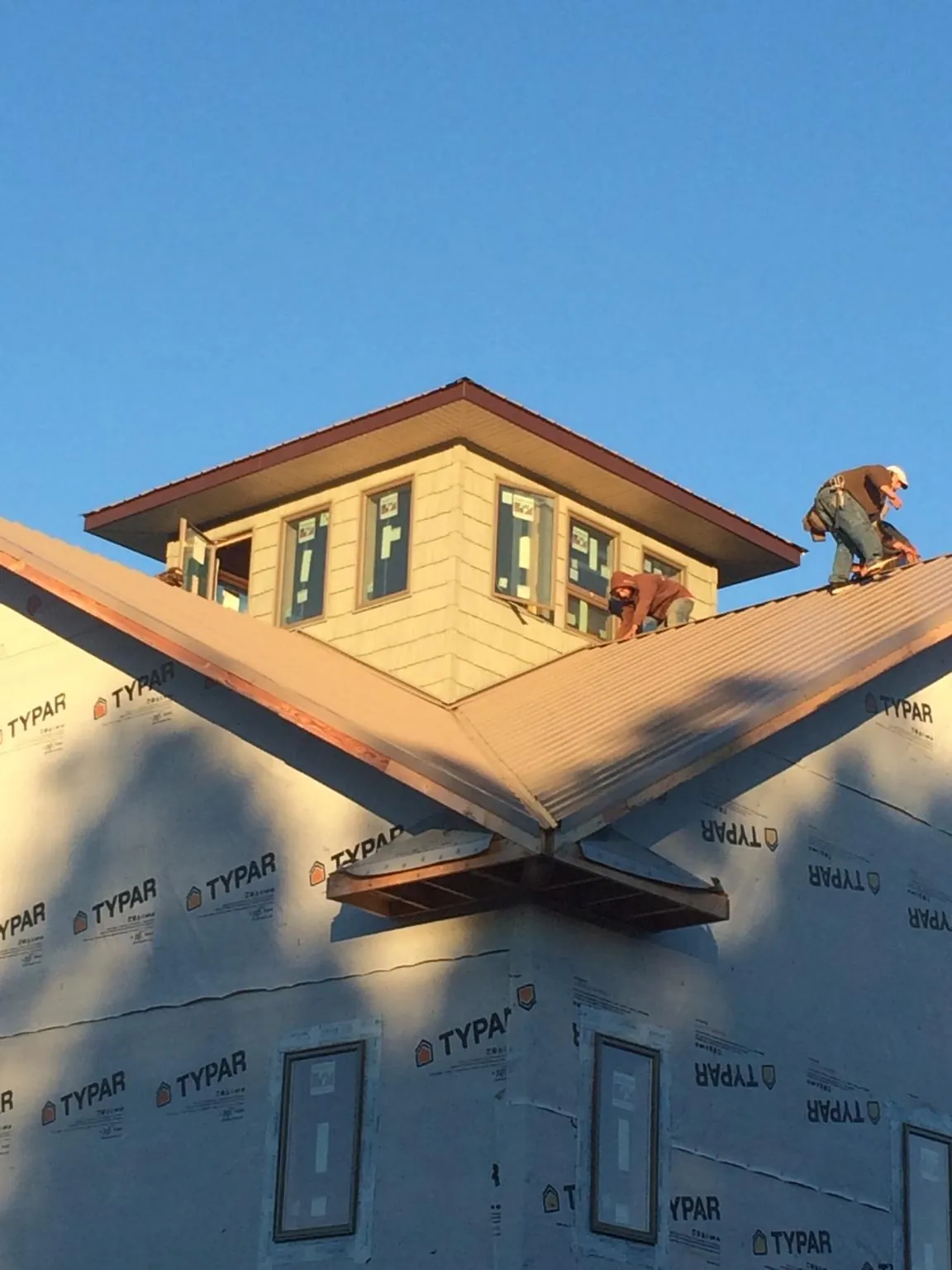 Roofers working around a rooftop cupola on a new metal roof at sunset — Roof Waterproofing in Falls by Roofing Brothers